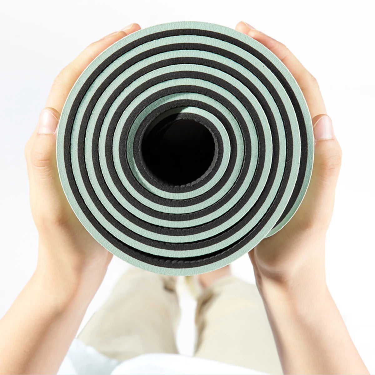 Rolled Flowna yoga mat held in two hands showing mint green and black TPE layers